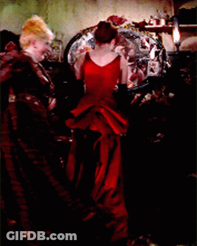 A Woman In A Long Red Dress Is Standing In Front Of A Mirror GIF