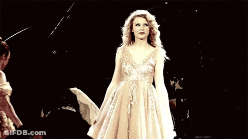 A Woman In A Long White Dress Is Dancing On A Stage In Front Of A Crowd . GIF