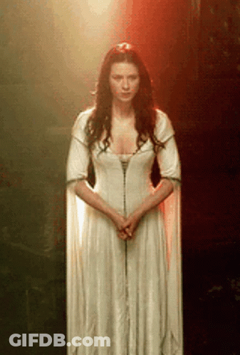 A Woman In A Long White Dress Is Standing In Front Of A Red Light . GIF