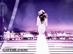 A Woman In A Long White Dress Is Standing On A Stage . GIF