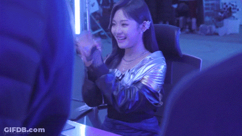 A Woman In A Metallic Jacket Is Sitting In A Chair In A Dark Room . GIF