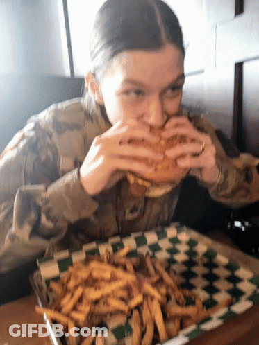 A Woman In A Military Uniform Is Eating A Sandwich And French Fries GIF