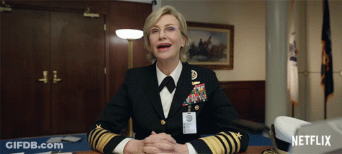 A Woman In A Military Uniform Sits At A Desk With A Netflix Logo In The Corner GIF