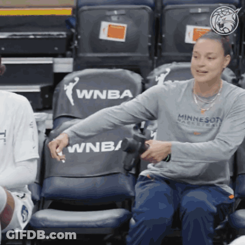 A Woman In A Minnesota Basketball Shirt Sits In A Bleacher GIF