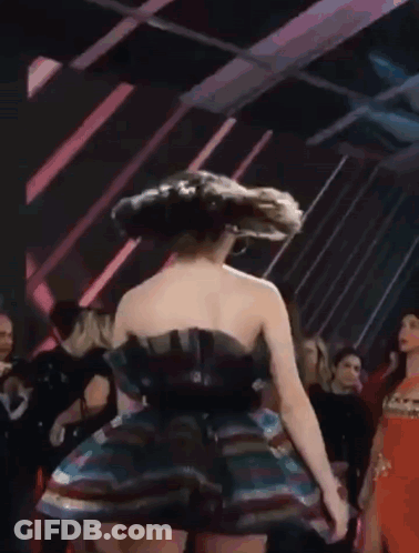 A Woman In A Multicolored Dress Is Dancing In A Crowd . GIF