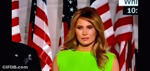 A Woman In A Neon Green Dress Is Standing In Front Of A Wall Of American Flags . GIF