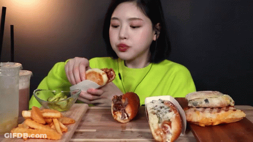 A Woman In A Neon Green Sweater Is Eating French Fries And Hamburgers GIF