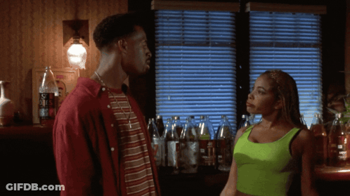 A Woman In A Neon Green Tank Top Stands Next To A Man In A Red Jacket GIF