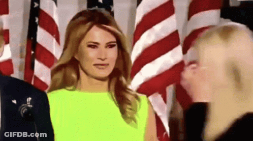 A Woman In A Neon Yellow Dress Is Standing In Front Of An American Flag . GIF