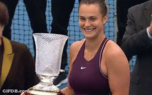 A Woman In A Nike Tank Top Is Holding A Trophy GIF