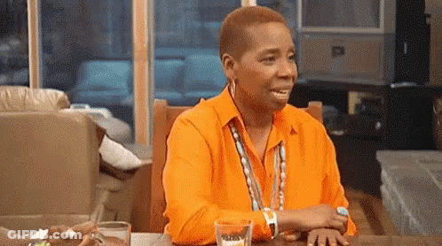 A Woman In A Orange Shirt Is Sitting At A Table With A Glass Of Water . GIF