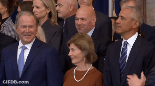 A Woman In A Pearl Necklace Stands Between Two Men In Suits And Ties GIF