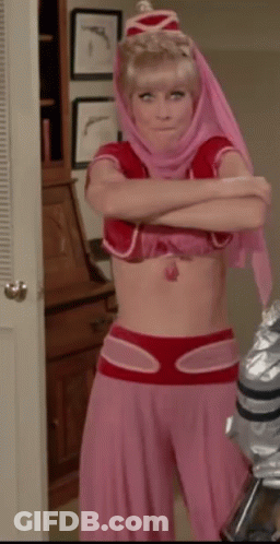 A Woman In A Pink And Red Costume With Her Arms Crossed Is Standing In A Room . GIF