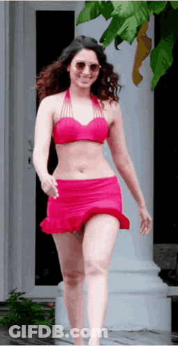 A Woman In A Pink Bikini And Red Skirt Is Walking Down A Sidewalk . GIF