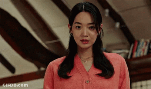 A Woman In A Pink Cardigan Is Standing In A Room . GIF