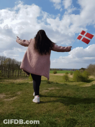 A Woman In A Pink Coat Holds A Red And White Flag In A Field GIF