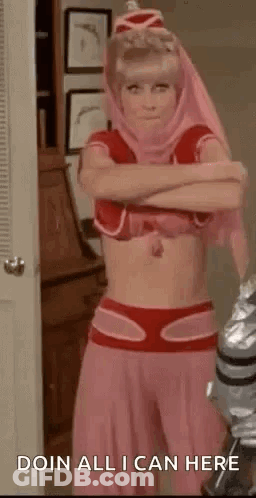 A Woman In A Pink Costume Is Standing In A Room With Her Arms Crossed And A Robot In The Background . GIF