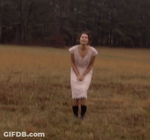 A Woman In A Pink Dress And Black Boots Stands In A Field GIF