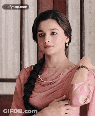 A Woman In A Pink Dress And Braided Hair Is Looking At The Camera . GIF