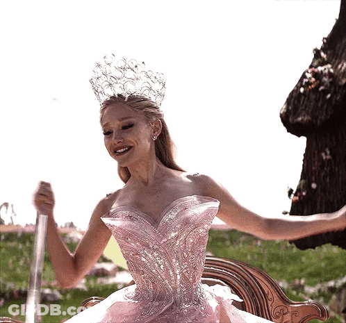 A Woman In A Pink Dress And Crown Is Holding A Wand GIF