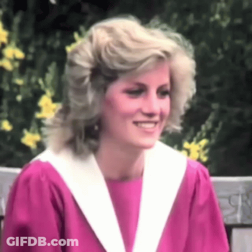A Woman In A Pink Dress And White Collar Is Smiling . GIF