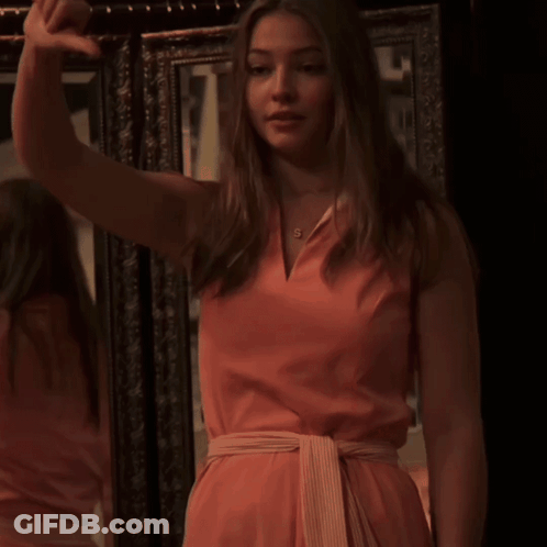 A Woman In A Pink Dress Has The Letter S On Her Necklace GIF