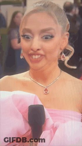 A Woman In A Pink Dress Holds A Microphone And Makes A Funny Face GIF