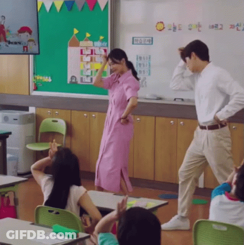 A Woman In A Pink Dress Is Dancing In A Classroom With A Sign That Says " Sun " On It GIF