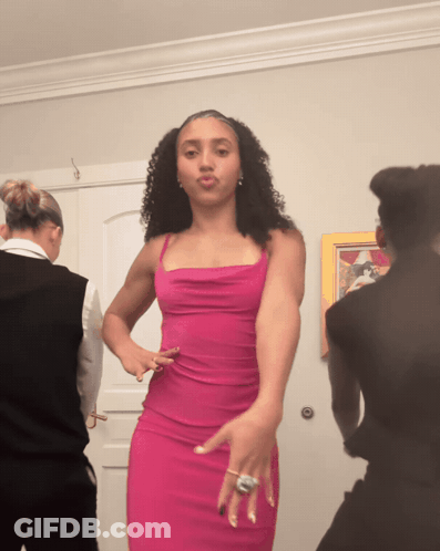 A Woman In A Pink Dress Is Dancing In Front Of A Door GIF