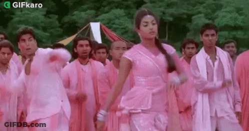 A Woman In A Pink Dress Is Dancing In Front Of A Group Of Men In Pink Clothes . GIF