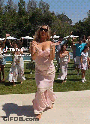 A Woman In A Pink Dress Is Dancing In Front Of A Group Of People With A Tik Tok Watermark GIF