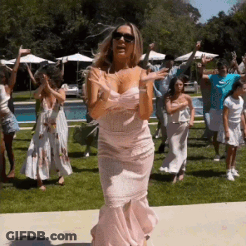 A Woman In A Pink Dress Is Dancing With A Group Of People In A Backyard . GIF