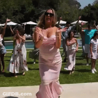 A Woman In A Pink Dress Is Dancing With A Group Of People In Front Of A Swimming Pool . GIF