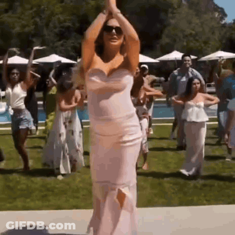 A Woman In A Pink Dress Is Dancing With A Group Of People . GIF