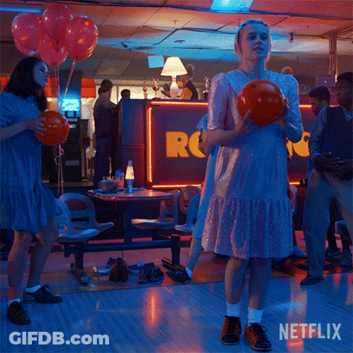 A Woman In A Pink Dress Is Holding A Bowling Ball In A Bowling Alley With Netflix Written On The Bottom GIF