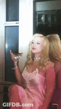 A Woman In A Pink Dress Is Holding A Glass Of Champagne GIF