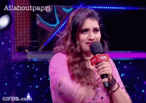 A Woman In A Pink Dress Is Holding A Microphone In Front Of A Sign That Says Allaboutpapri GIF
