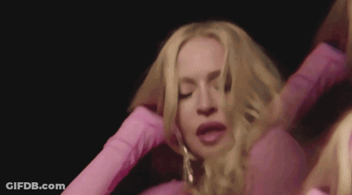 A Woman In A Pink Dress Is Holding Her Hair In Her Hands . GIF