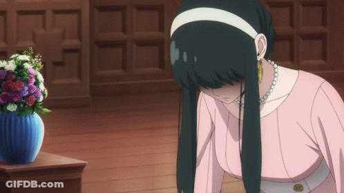 A Woman In A Pink Dress Is Kneeling Down In Front Of A Blue Vase Of Flowers GIF