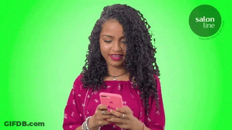 A Woman In A Pink Dress Is Looking At Her Cell Phone GIF