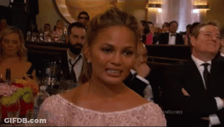 A Woman In A Pink Dress Is Making A Funny Face While Sitting In A Crowd Of People . GIF
