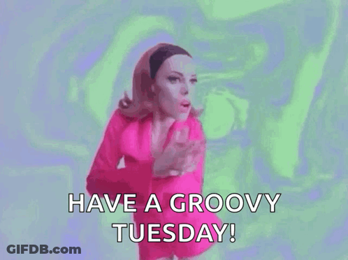 A Woman In A Pink Dress Is Saying `` Have A Groovy Tuesday '' . GIF
