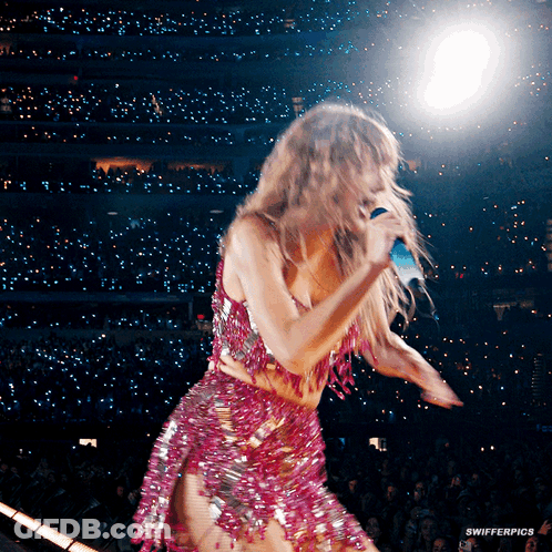 A Woman In A Pink Dress Is Singing Into A Microphone On A Stage GIF