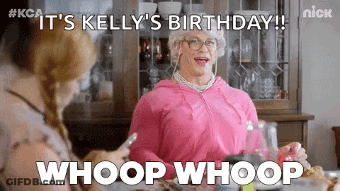 A Woman In A Pink Dress Is Sitting At A Table With A Woman In A Wig And Glasses . GIF