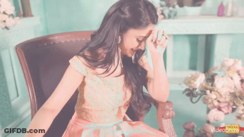 A Woman In A Pink Dress Is Sitting In A Chair And Covering Her Face With Her Hands GIF