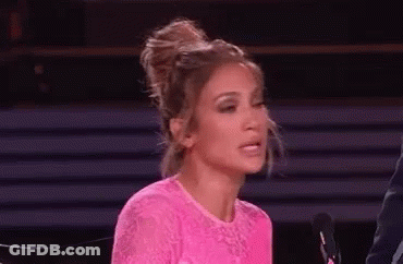 A Woman In A Pink Dress Is Sitting In Front Of A Microphone And Making A Face . GIF