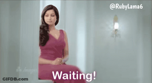 A Woman In A Pink Dress Is Sitting In Front Of A Wall That Says Waiting GIF