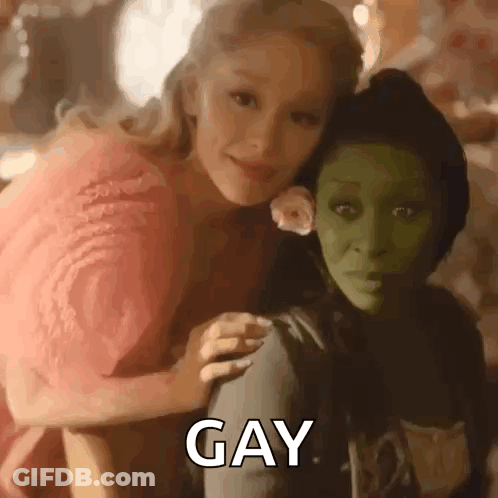 A Woman In A Pink Dress Is Sitting Next To A Green Woman In A Green Mask . GIF