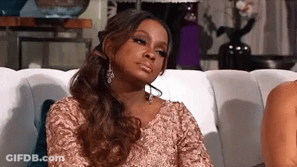 A Woman In A Pink Dress Is Sitting On A Couch Making A Funny Face . GIF