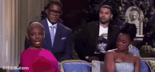 A Woman In A Pink Dress Is Sitting On A Couch Next To Two Men In Suits . GIF